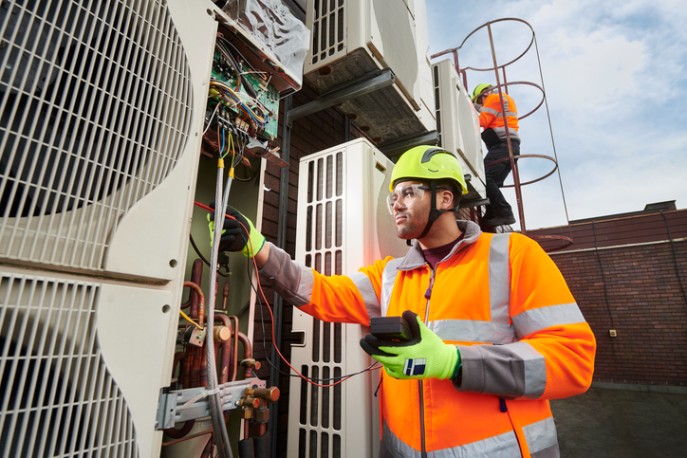 A service worker in an orange safety vest performs maintenance on an HVAC unit in DuPage County, IL