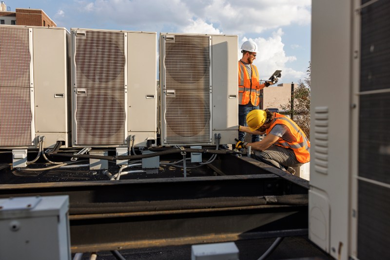 Two technicians performing spring maintenance on a commercial AC unit in DuPage County, IL